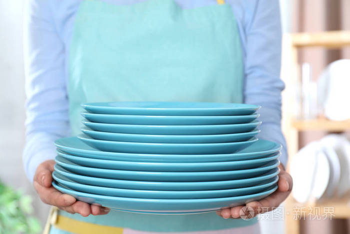女人拿着一叠干净的盘子在模糊的背景上靠近