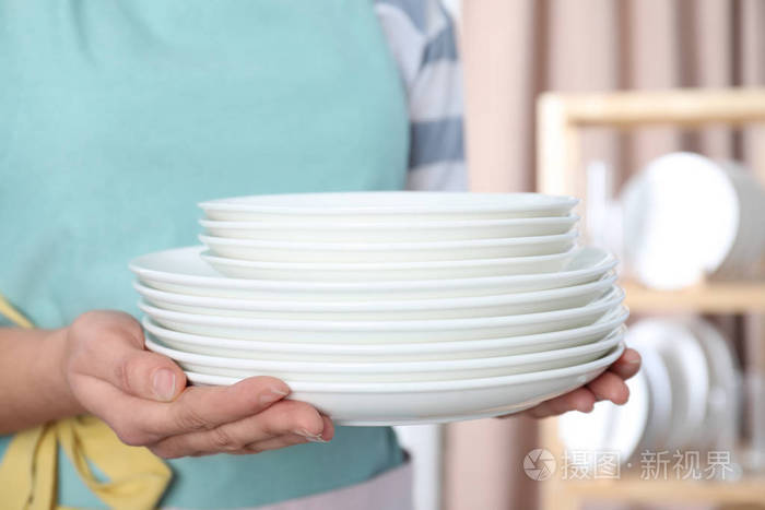 女人拿着一叠干净的盘子在模糊的背景上靠近