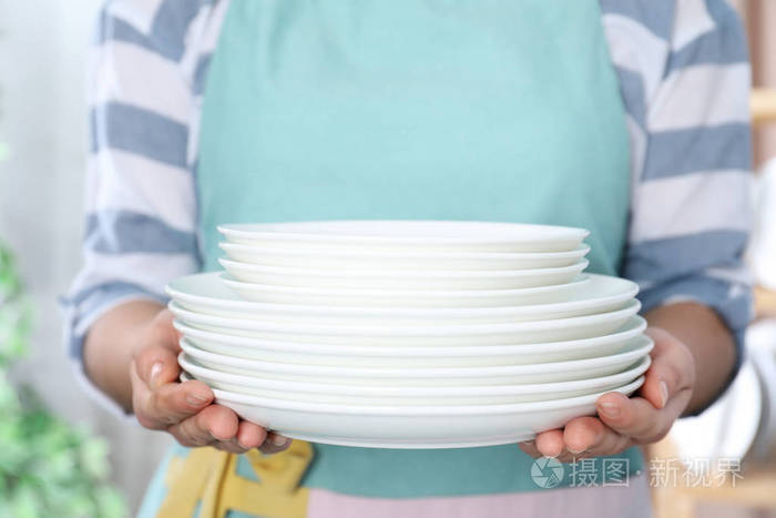 女人拿着一叠干净的盘子在模糊的背景上靠近