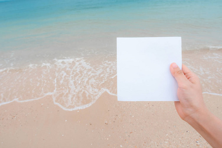 女人手拿白纸，海滩和软波背景。