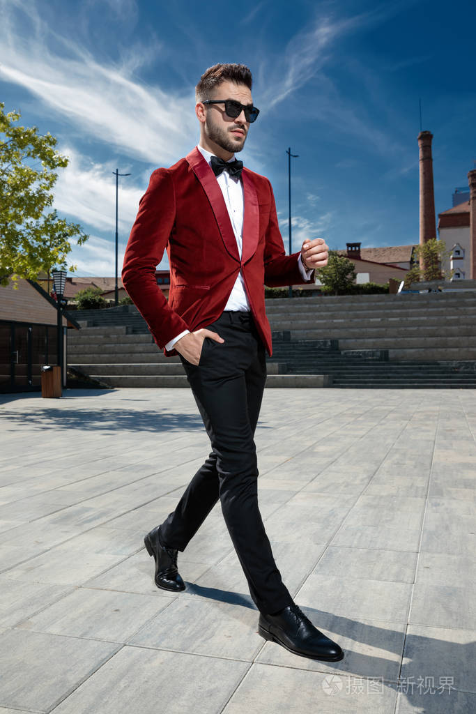一个傲慢的年轻人穿着红色天鹅绒晚礼服走在户外