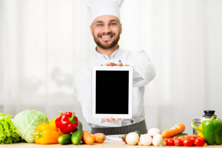 快乐的厨师在厨房向摄像机展示数字平板电脑屏幕