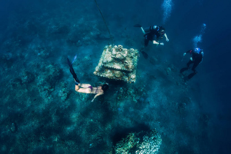 Young woman free diver glides with fins near underwater temple. 