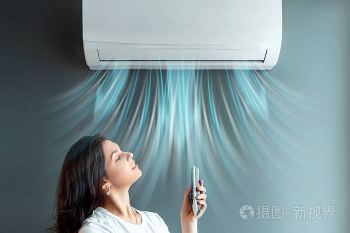 一个漂亮的女孩站在空调和一股新鲜的冷空气下靠着灰色的墙壁概念热冷