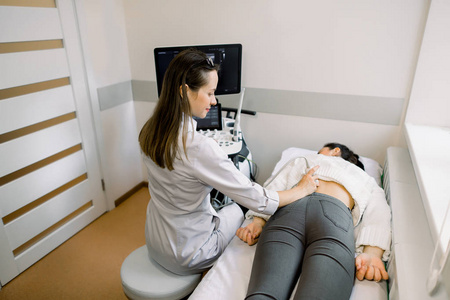 超声波在物理治疗中的应用。年轻女性治疗师使用超声波扫描仪对女性患者下背部进行检查。背部和肾脏超声
