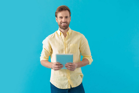 Happy casual man holding a tablet and looking forward 