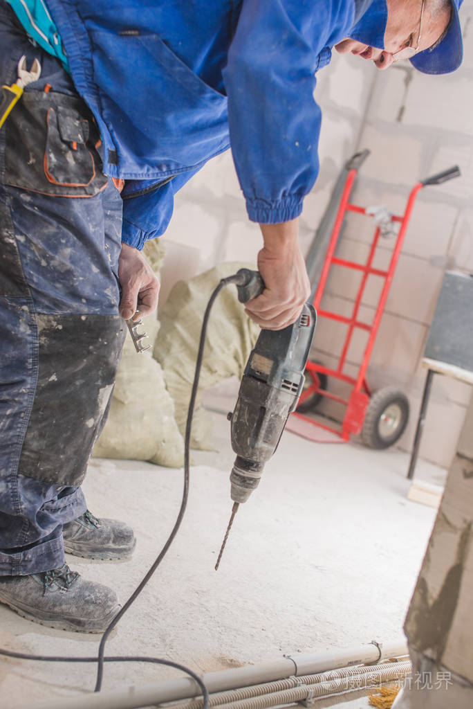 家庭维修男性手用电钻和钻头在墙上打一个洞油漆剥落