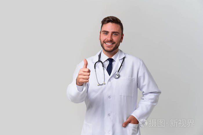 年轻英俊的现代医生穿着白色的医疗袍站在工作室的白色背景上。医科大学的见习生。