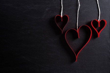 Red paper hearts hanging on ropes on black background. Love and 