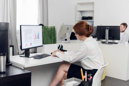 上班族,穿着裙子的女人坐在桌子旁写东西照片