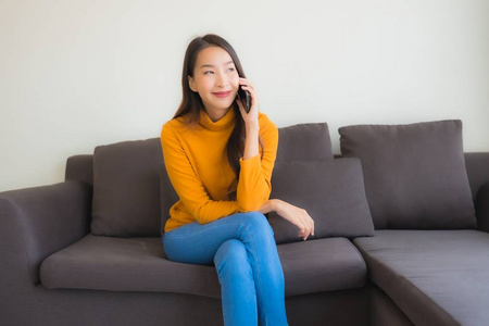 年轻的亚洲女性在沙发上使用智能手机