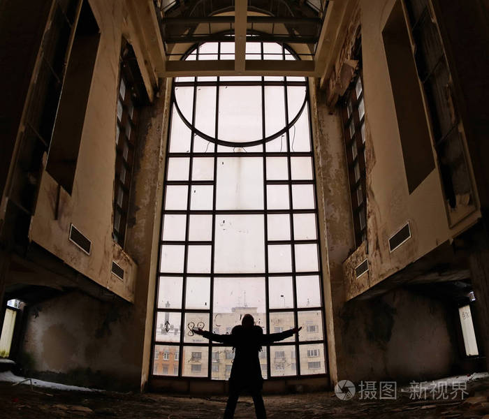 一个破旧的废弃旅馆大厅里的大窗户上的男人剪影