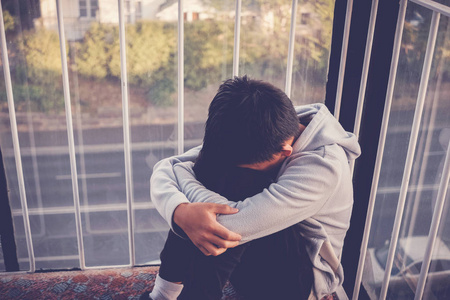 Depressed young preteen teenage boy hugging his knee , children 