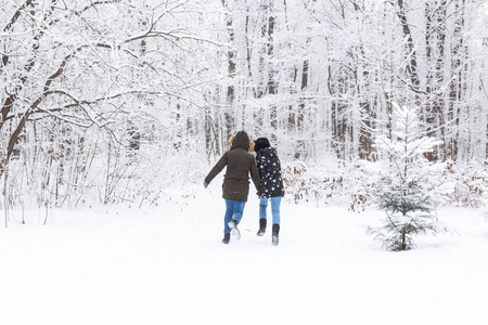 一对年轻漂亮的情侣在雪地公园里嬉戏，奔跑着，手牵着手。情人节概念。冬季。