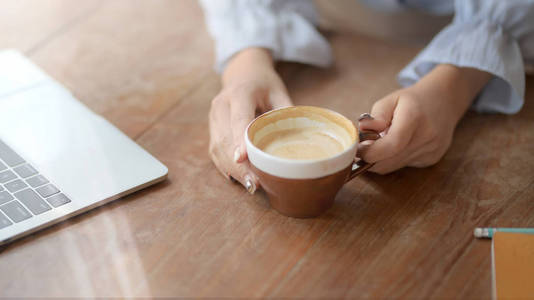 一个女人拿着咖啡杯，在舒适的工作场所拿着笔记本电脑和文具