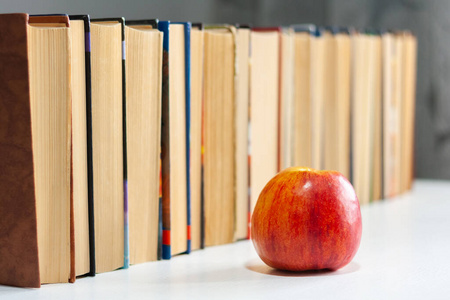 一摞精装书放在白桌子上,桌上放着红苹果.图书站照片