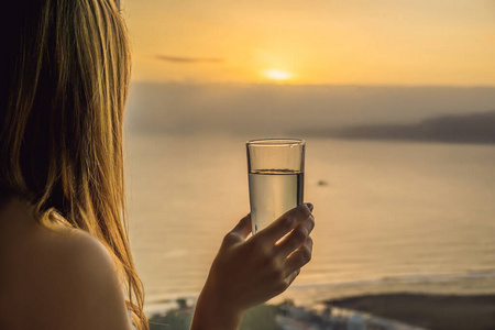 女人早上在一扇可以看到海景的窗户的背景上喝水