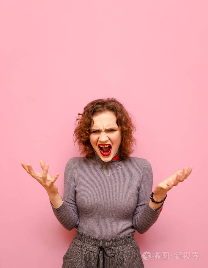 一个情绪激动的女孩穿着时髦的休闲服卷发粉色背景看