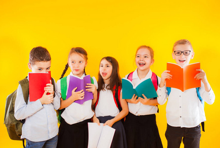 快乐兴奋微笑的小学生拿着孤立在黄色背景上的彩书。回到学校。