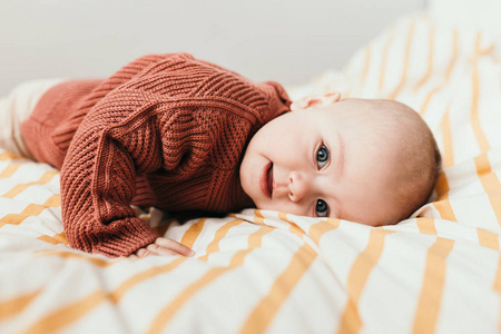 漂亮的小女孩在床上穿着舒适的棕色毛衣微笑。母性和童年的概念