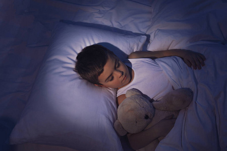 小男孩和泰迪熊在家睡觉.就寝时间照片