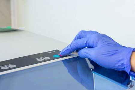 戴蓝色手套的女士按化学或实验室设备上的启动按钮。