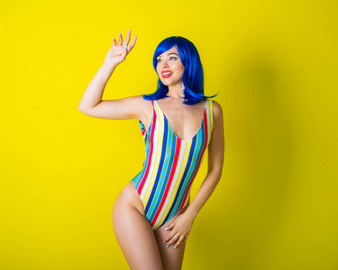 身穿条纹泳衣，戴蓝色假发，在黄色背景下摆姿势的美女。一个迷人女孩的肖像。