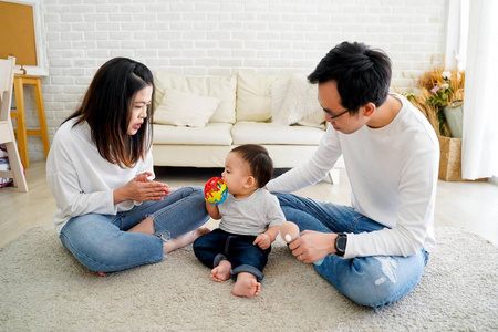 一个亚洲家庭，父母在家里和儿子坐在地板上玩玩具娃娃