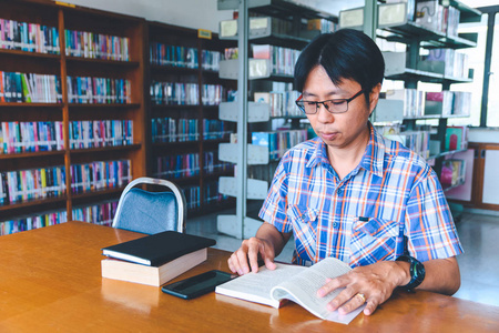 微笑的亚洲男子学生在图书馆工作
