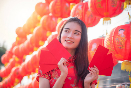 身着中国传统服装的美丽亚洲女孩在中国红灯笼前微笑着拿着红包钱