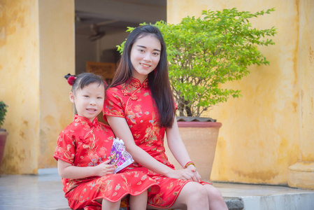 小女孩和妈妈穿着中国传统服装坐在家门口，开心地笑着。