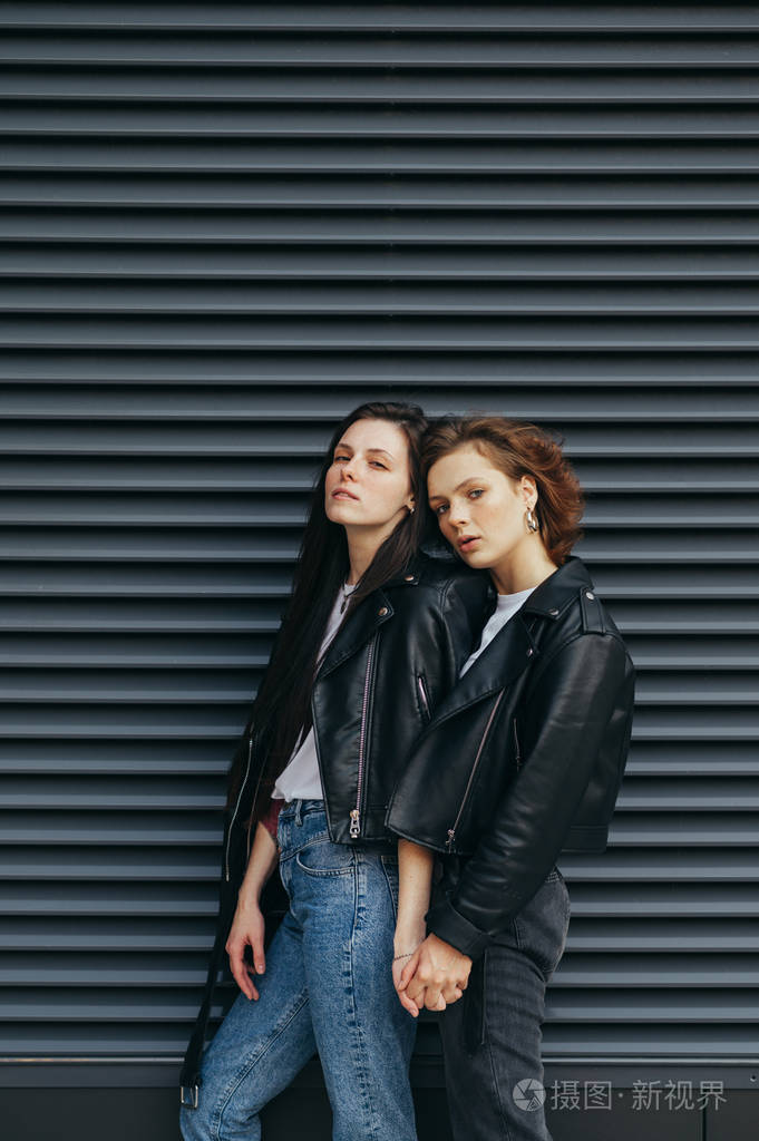 两位时尚休闲装模特站在黑色背景上一脸严肃地看着镜头两个穿皮夹克的