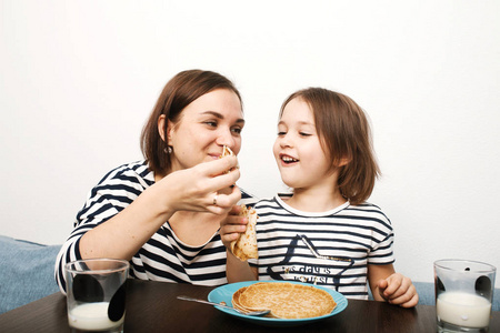 妈妈和小女儿早上在明亮的厨房里吃着牛奶煎饼，开心地笑着