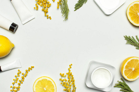 白色化妆品瓶容器与黄色含羞草花和新鲜柠檬在灰色背景俯视图平放。化妆品水疗品牌模型，天然有机美容产品概念维生素C