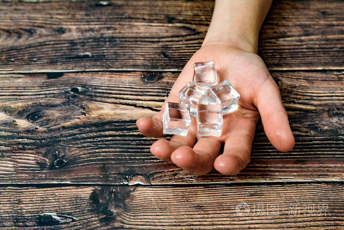 男人伸出手来手里拿着冰块背景是黑色的木头