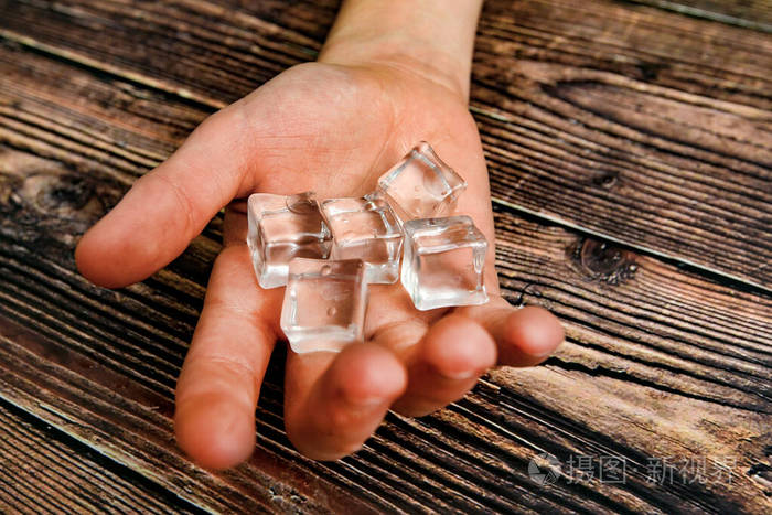 男人伸出手来手里拿着冰块背景是黑色的木头