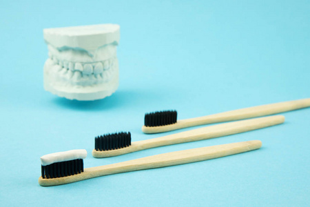 竹牙刷和天然牙膏躺在蓝色的背景和旁边的石膏模型下巴。口腔护理正畸医师。