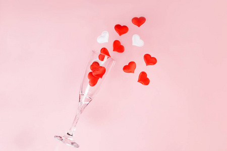 一杯香槟，粉红色背景上洒着红白相间的心形五彩纸屑