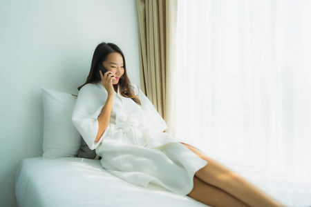 年轻的亚洲女人在床上用智能手机