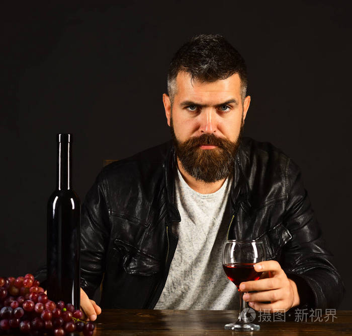 严格把脸的除气器坐在酒瓶和葡萄旁