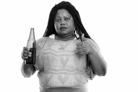 摄影棚拍摄的非洲黑人胖女人拿着一瓶啤酒,竖起大拇指照片