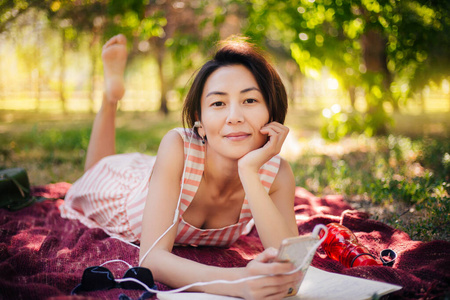 这个女孩躺在草地上，在笔记本上读讲座。一个女人在公园里看书，听音乐。户外教育