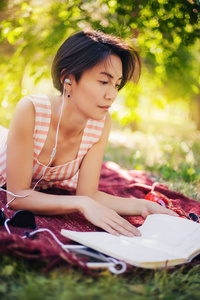 这个女孩躺在草地上，在笔记本上读讲座。一个女人在公园里看书，听音乐。户外教育