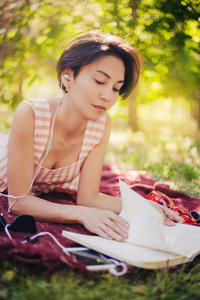 这个女孩躺在草地上，在笔记本上读讲座。一个女人在公园里看书，听音乐。户外教育