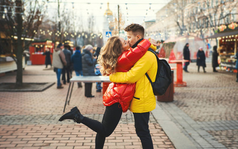 恋爱中的浪漫情侣亲吻，拥抱，走在街上，穿着鲜艳的羽绒服。城市背景。