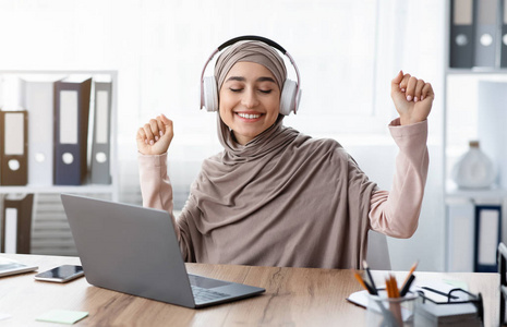 快乐的阿拉伯女人用无线耳机听音乐，在工作场所放松