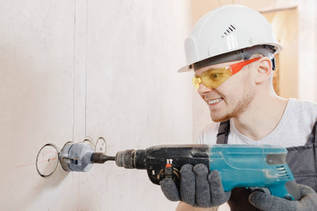 建筑工人用风锤在混凝土砖墙上钻孔,钻石冠,用于电缆,插座,开关照片