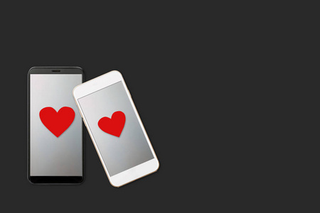 在黑暗的背景下，两部屏幕上有心形图案的智能手机，现代小玩意爱与关系爱的信息情人节的概念