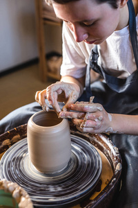 陶工在陶工的轮子上做花瓶。在一个车间里，一个女人用手在制作罐子。