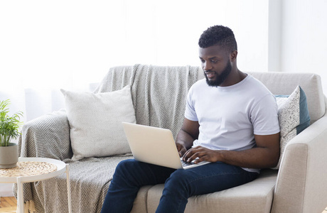 年轻的非洲男人在家里用笔记本电脑工作